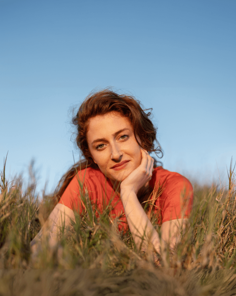 Woman resting on grass, smiling at camera.